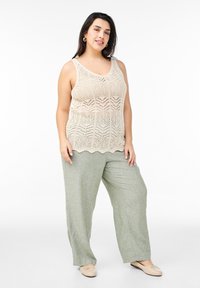 Beige Spitzenstrick-Tanktop mit gewelltem Saum, kombiniert mit lockeren, hellgrünen Leinenhosen. Das Outfit bietet weiche Texturen und eine entspannte Passform.