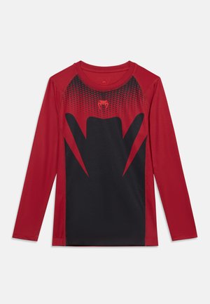 T-shirt de sport rouge à manches longues avec des motifs géométriques noirs et un petit logo serpent rouge au centre de la poitrine.
