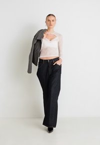 Μαύρα μακριά τζιν με ελαφριά φουσκωτή γραμμή, σε συνδυασμό με ένα διάφανο λευκό τοπ και ένα γκρι σακάκι που ακουμπά πάνω σε έναν ώμο, αναδεικνύοντας μία εφαρμοστή σιλουέτα.