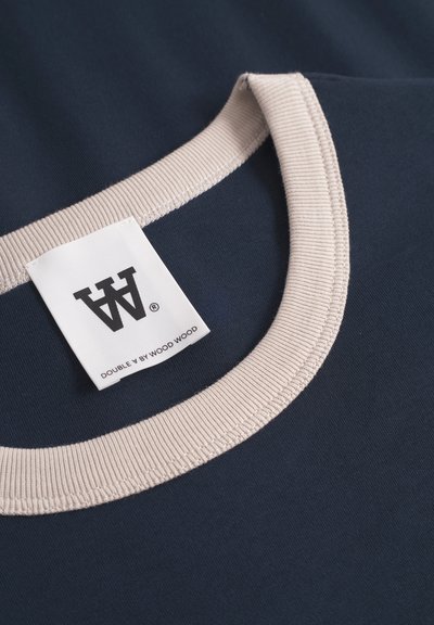 Ναυτικό T-shirt με ανοιχτό μπεζ ριμπ λαιμό και ορατή εσωτερική ετικέτα, κατασκευασμένο από λείο βαμβακερό ύφασμα. Καθαρός, απλός σχεδιασμός.