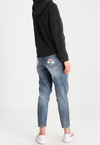 Svart huoodjacka, ljusblå slitna jeans med regnbåge och moln broderi på bakfickorna, vita sneakers med blommiga detaljer.