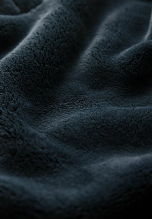 Tumehall sinine plüüštekitaal, millel on pehme tekstuuriga pind, näidates õrnu voldid ja laineid, rõhutades selle hubast välimust.