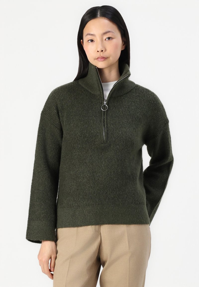 Dunkelgrüner, gestrickter Pullover mit einem halben Reißverschlusskragen und entspannter Passform. Mit langen Ärmeln sowie gerippten Bündchen und Saum.
