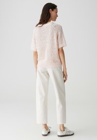 Maglione a maniche corte in maglia di colore rosa chiaro con finitura texturizzata, abbinato a pantaloni bianchi a gamba dritta e sneakers grigie.