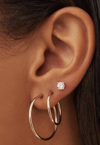 Roze gouden oorbellen in de vorm van een grote ring met een glanzende, ronde diamantstud. De ringen zijn groot en de stud is gezet in een mount met vier pootjes.