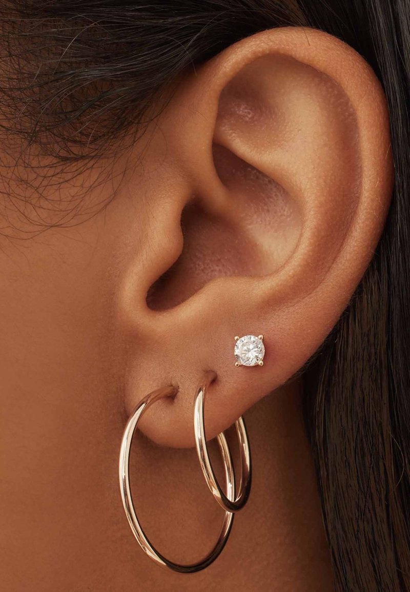 Roze gouden oorbellen in de vorm van een grote ring met een glanzende, ronde diamantstud. De ringen zijn groot en de stud is gezet in een mount met vier pootjes.