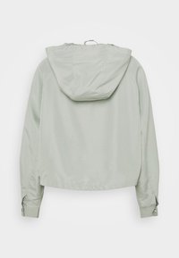 Jasnoszara kurtka typu cropped z kapturem, z długimi rękawami i zatrzaskowymi zapięciami na mankietach. Gładki, syntetyczny materiał o matowym wykończeniu.