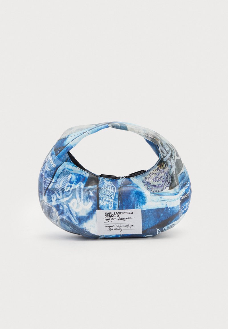 Blue fabric handbag with curved handle, featuring a mix of denim patterns, floral accents, and printed text. Tag displays brand details.