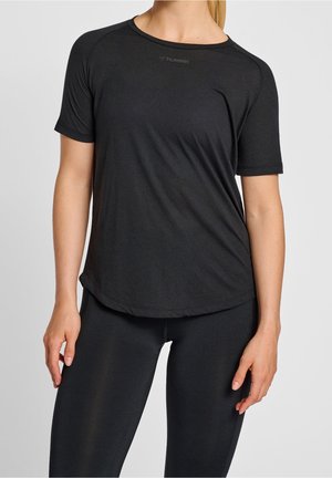 Frau trägt ein schwarzes hummel-Sport-T-Shirt mit kurzen Ärmeln und schwarze Leggings, steht vor einem schlichten hellen Hintergrund.