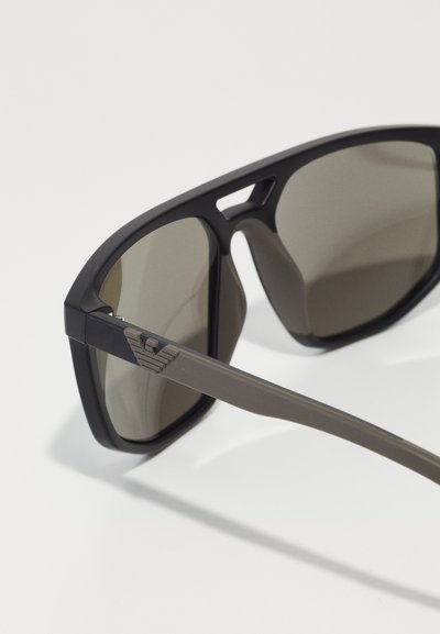 Ochelari de soare negri cu lentile gri. Design cu ramă pătrată și finisaj mat. Accentuate cu un logo pe braț. Evidențiind o construcție robustă.