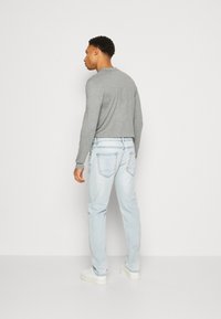 Gray long-sleeve shirt, light blue jeans with visible stitching, and white sneakers. Casual outfit viewed from the back against a plain background.