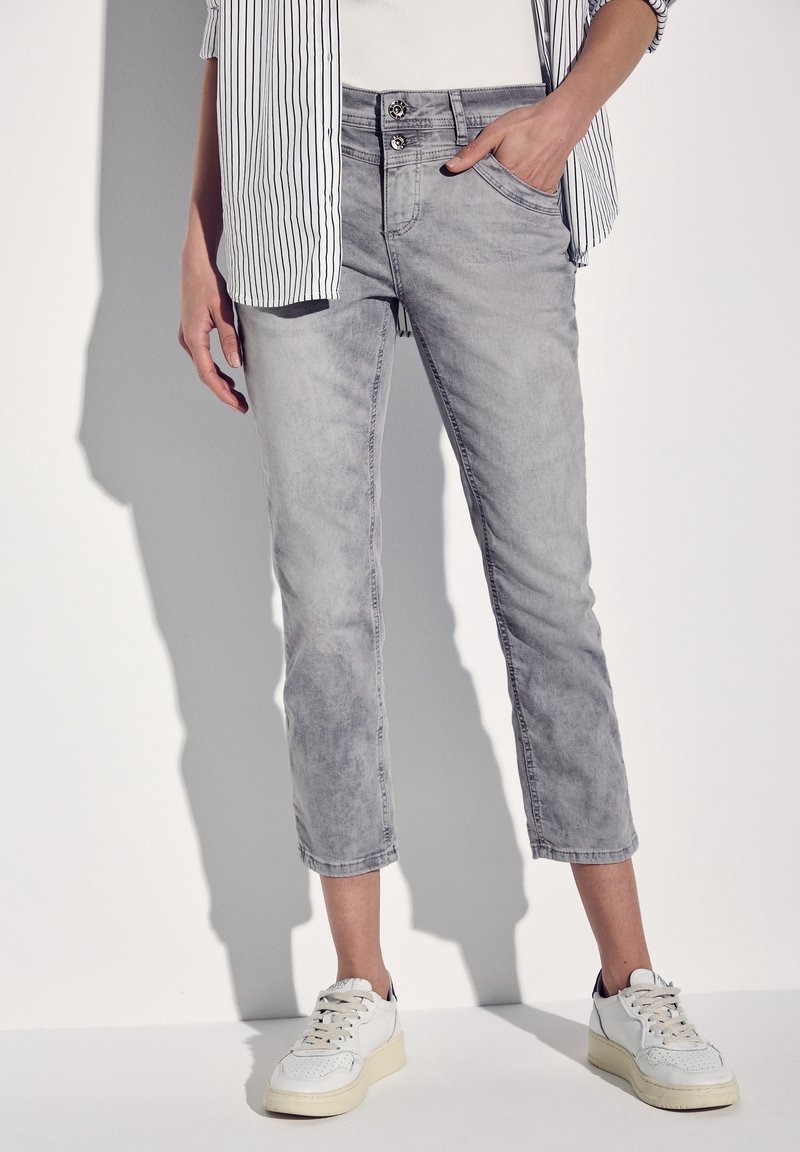 Gray denim cropped jeans with a faded finish, button closure, and five-pocket design, paired with white sneakers and a striped shirt.