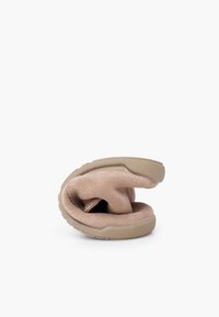 Beige suede shoe flexed to show its soft, flexible sole and upper, against a plain white background.