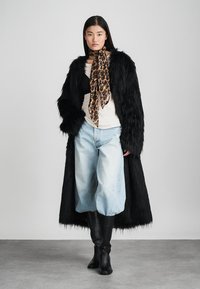 Μακρύ μαύρο ψεύτικο παλτό από γούνα, μπεζ μπλούζα, ανοιχτού μπλε φαρδιά παντελόνια και μαύρες μπότες μέχρι το γόνατο. Διακοσμημένο με μαντήλι λεοπάρ.