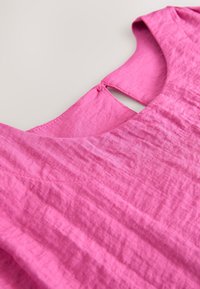 Pink linen top with a round neckline and a keyhole opening at the back. Features subtle texture and stitching details throughout.