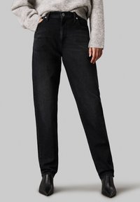 Vaqueros negros de tiro alto, hechos de denim, con bolsillos frontales, cierre de botón y diseño de pierna recta.