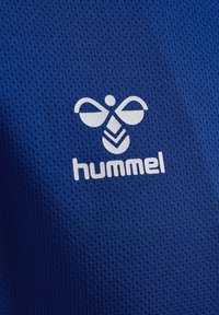Blå net sports-trøje med en hvid logo og teksten "hummel" nederst. Teksturen er åndbar med et mønstret finish.