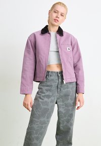 Lavendel geknipte jas met een zwarte kraag, voorzien van een voorkant rits en een borstzak. Grijs patroonde wijd-uitlopende jeans maken de outfit compleet.