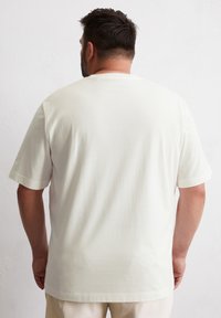 Kremowy t-shirt z krótkim rękawem, luźny krój, wykonany z miękkiej bawełny. Posiada standardowy okrągły dekolt i gładką teksturę.