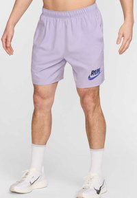 Pantalones cortos deportivos de color púrpura claro con una cinturilla elástica, que presentan un logo "RUN" en azul oscuro y un swoosh de Nike. Llevados con zapatos y calcetines blancos.