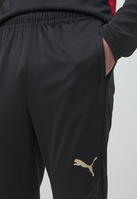 Black athletic pants made of lightweight fabric, featuring an elastic waistband, side pockets, and a gold Puma logo on the left thigh.