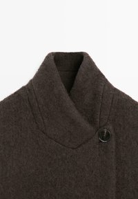 Tmavě hnědý vlněný kabát s širokým šálovým límcem a jedním velkým černým knoflíkem u krku, zobrazený na bílém pozadí.