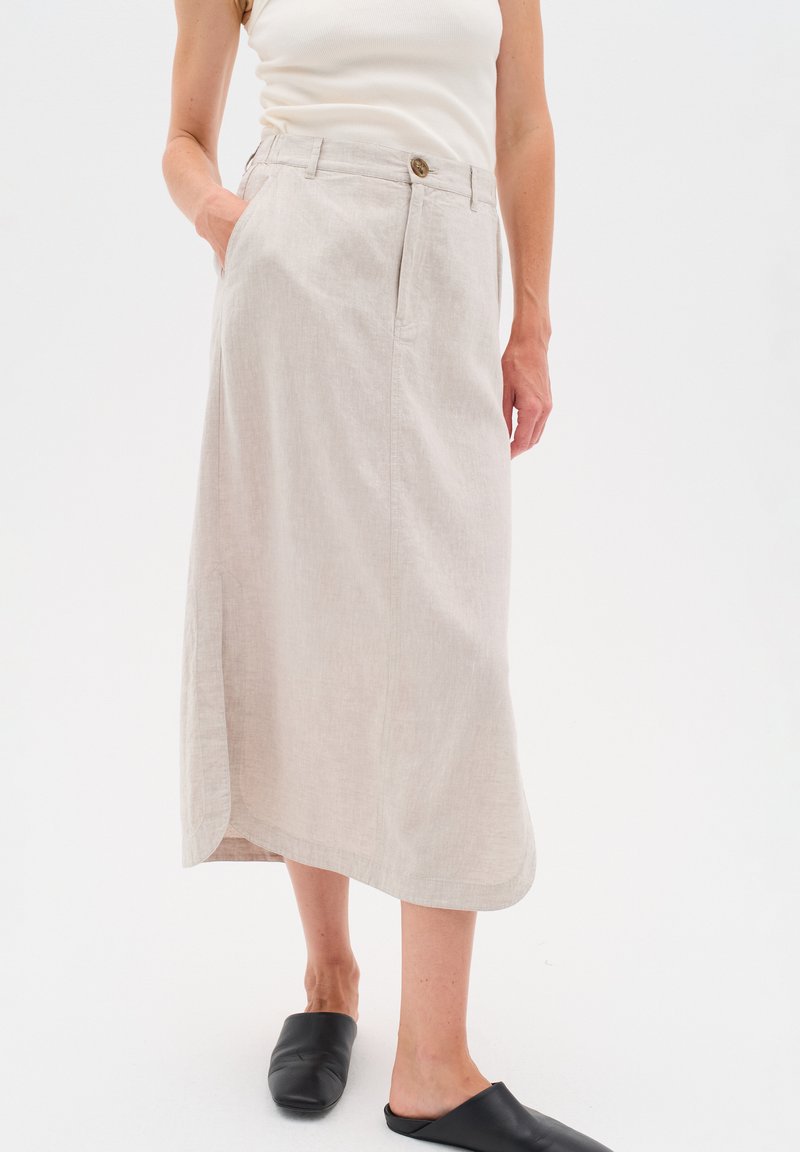 Vaal beige linnen rok met een zijsplit, twee zakken, een knoopsluiting aan de voorkant en een relaxte pasvorm. Gecombineerd met zwarte instapschoenen.
