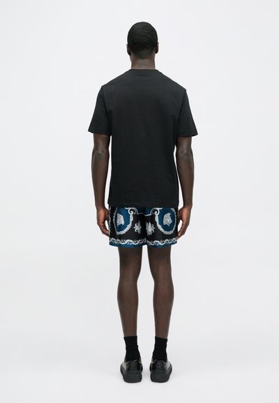 Czarny t-shirt z krótkim rękawem w połączeniu z wzorzystymi niebiesko-czarnymi szortami z białymi i jasnoniebieskimi akcentami, czarnymi skarpetkami do kostki oraz butami.