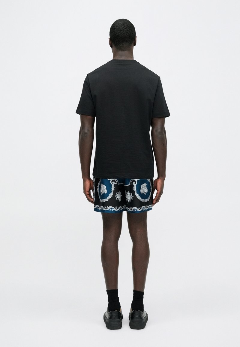 Black short-sleeve t-shirt paired with patterned blue and black shorts featuring white and light blue accents, black ankle socks, and shoes.