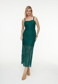 Tiffanyblaues Spitzenkleid mit tailliertem Oberteil und Spaghettiträgern, das einen transparenten, bodenlangen Rock hat. Goldene Sandalen und Schmuck runden den Look ab.