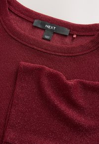 Vinrød ribstrikket sweater med tekstureret finish. Har rund hals og en etiket med teksten "NEXT" samt subtile glinsende detaljer over hele sweateren.