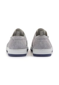 Des chaussures slip-on en toile gris clair avec des semelles en caoutchouc blanc, présentant une surface texturée et des accents contrastants en bleu marine sur la semelle.