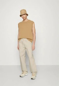 Bež pleteni bezrukavnik, svijetlosmeđe široke hlače i krem tene s bež naglasima, upotpunjeni bež šeširom sa širokim obodom.