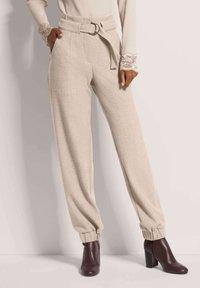 Beige wijde broek met een aansluitende taille, riem met een metalen gesp en manchetten aan de enkels. Zachte textuur, op maat gemaakte pasvorm, zijzakken.