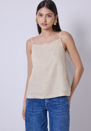 Beige lněná tílko s tenkými ramínky, vlnkovým výstřih a volným střihem, spolu s modrými džínami. Minimalistický design.