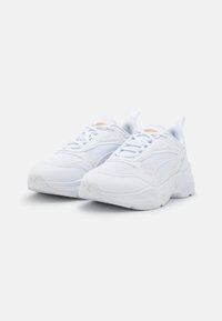 Scarpe sportive bianche con tomaia in mesh e materiale sintetico, suola spessa, collo imbottito e cuciture tonali. Presentano un'etichetta di pull e piccoli dettagli con logo.