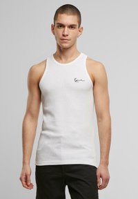 Weißes ärmelloses Tanktop aus gerippter Baumwolle, mit rundem Halsausschnitt und kleinem schwarzem Logo auf der Brust.