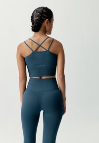 Turkos sport-bh med korslagda band och ribbad textur; turkosa högmidjade leggings med diagonala mönster och sömlös design.