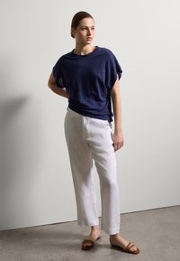 Marineblaues lässiges Oberteil, kombiniert mit weißen Leinenhosen und braunen Schlappen, mit einem schlichten Design und weichen Texturen.