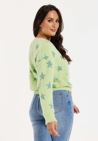 Fuzzy green sweater with blue star patterns, round neckline, and long sleeves. Paired with blue jeans, showcasing a fitted silhouette.