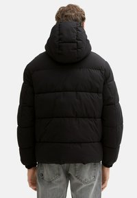 Giacca a vento nera con cappuccio, design trapuntato con strisce orizzontali, polsini elasticizzati e texture liscia.