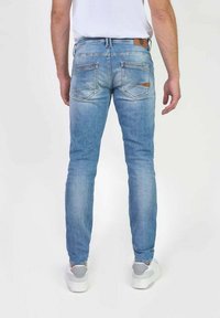 Jeans ajustados de color azul claro con un acabado desgastado, que cuentan con bolsillos traseros con parche y un detalle de cuero marrón en la cinturilla.