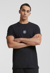 Zwarte katoenen T-shirt met korte mouwen, voorzien van een rond logo op de borst. De pasvorm is relaxed en de stof lijkt glad.