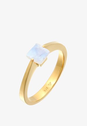 Złoty pierścionek z przezroczystym, kwadratowym kamieniem księżycowym, osadzony w minimalistycznym wzornictwie z gładką obrączką i polerowanym wykończeniem.