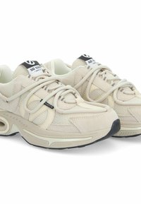 Beżowe buty sportowe wykonane z materiałów mesh i zamszowych, z grubą podeszwą, okrągłym noskiem oraz krzyżującym się sznurowaniem z etykietą marki na języku.