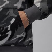 Camo-mønstrede sweatshirts i nuancer af sort og grå, med en frontlomme, ribbede manchetter og en afslappet pasform. Sølv kædearmbånd synligt.