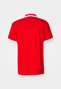 Camisa polo roja con un ribete blanco en el cuello, de mangas cortas y una textura de tela suave. Presenta un corte recto y un diseño simple.