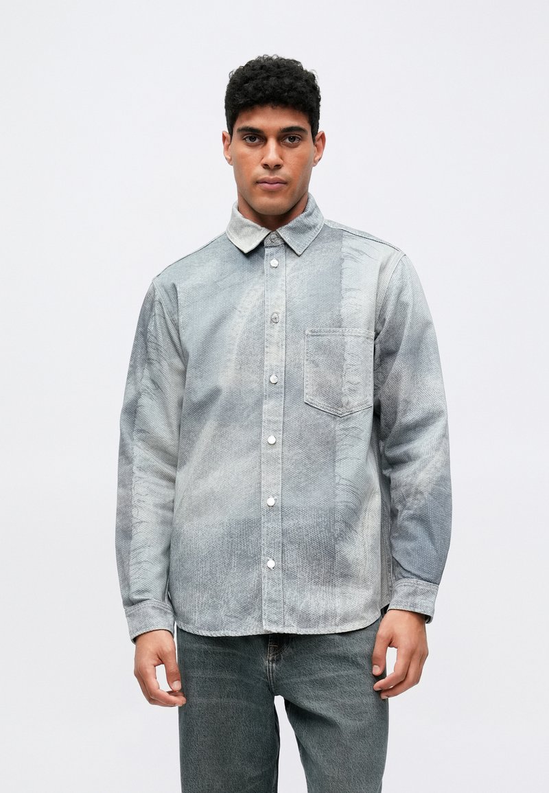 Džínová košeľa s vyblednutou svetlomodrou a šedou farebnou paletou, s golierom na zapínanie, prednou vreckom a textúrovanou látkou.