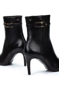 Botines de cuero negro hasta el tobillo con tacones afilados, que presentan detalles de hebillas doradas y una textura suave y brillante. Detalle del logo en el caña.