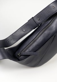 Borsa a tracolla in pelle blu navy con tracolla regolabile, chiusura a cerniera e superficie liscia. Include una piccola tasca frontale con linguetta.